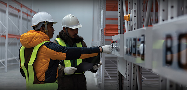 Two workers wearing protective clothing in a refridgerated warehouse.