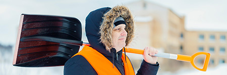 A man in cold weather clothing holds a snow shovel.